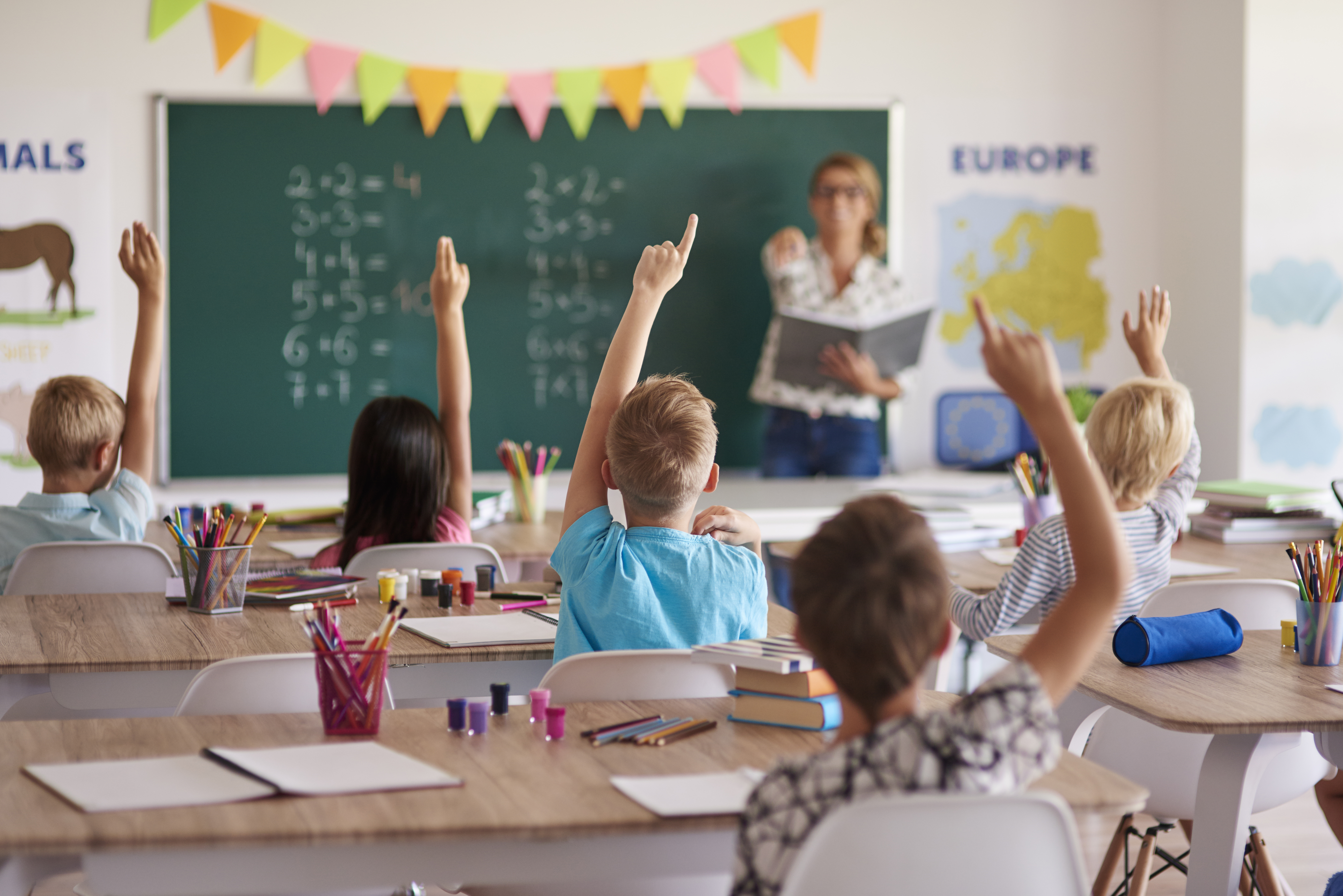 Immagine raffigurante una classe di bambini che alzano la mano